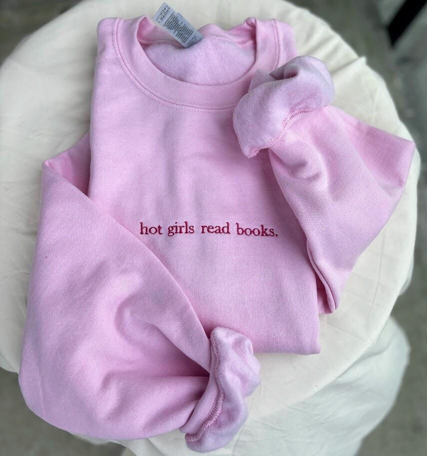 Embroidered sweatshirt with the phrase "Hot Girls Read Books" in stylish script. Cozy and chic, this sweatshirt celebrates book lovers with a bold statement. Perfect for bibliophiles who embrace both style and intellect. In various colors and sizes.
