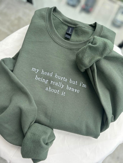 Military Green Embroidered Sweatshirt. Text says &quot;my head hurts but i&#39;m being really brave about it&quot;.